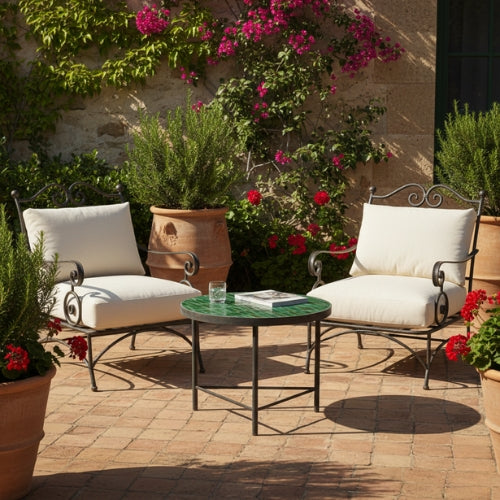 Table basse ronde en zellige marocain vert avec pied droit en fer forgé installée dans un salon de jardin extérieur