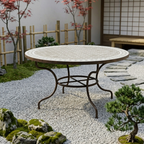 Table ronde en zellige beige Ø150 cm installée sur terrasse extérieure avec pied en fer forgé rouillé