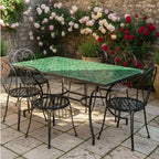 Table rectangulaire en zellige marocain vert avec pied fixe en fer forgé noir installée dans un jardin extérieur