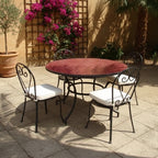 Table ronde en zellige marocain bordeaux avec pied fixe en fer forgé noir installée dans un jardin extérieur