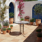 Table ronde en zellige marocain multicolore avec pied fixe en fer forgé noir installée sur terrasse extérieure